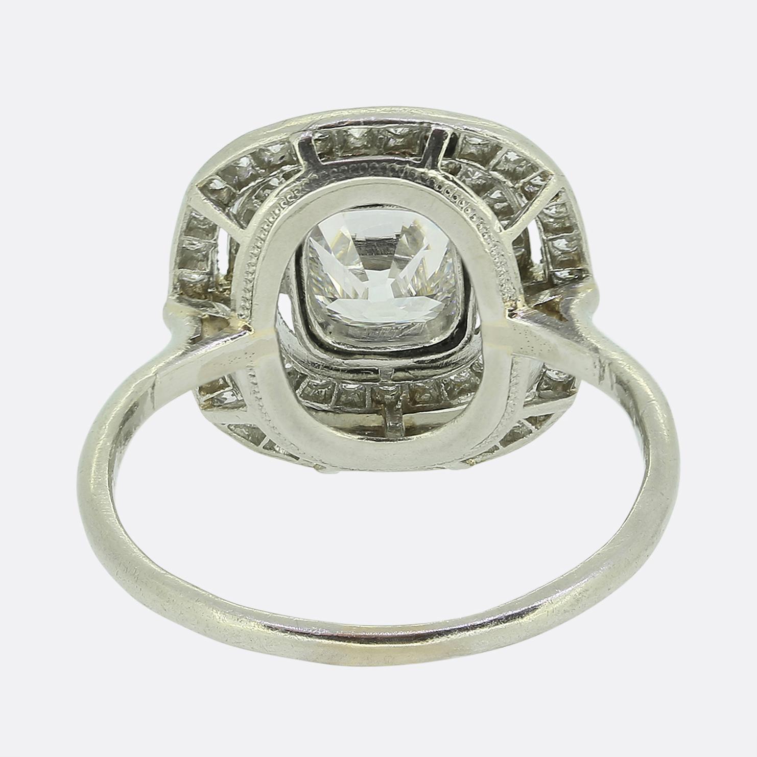 Ecco uno squisito anello a grappolo tratto dall'apice del movimento Art Déco. Al centro del quadrante troviamo un antico diamante con taglio a cuscino, circondato da una doppia aureola aperta di diamanti bianchi brillanti tagliati da miniera. Le