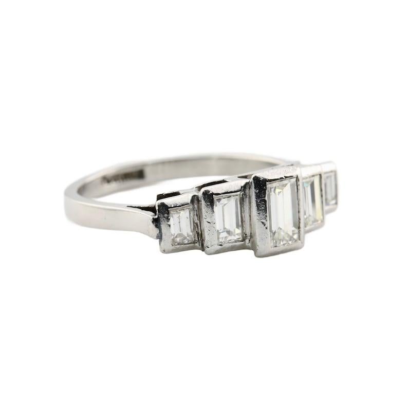 Aston Estate Jewelry Presents:

An Art Deco period baguette cut diamond band ring in platinum. Set with five graduated baguette cut diamonds in a stepped formation. Weighing 0.40 carats, the largest center diamond is framed by a pair of 0.25 carat