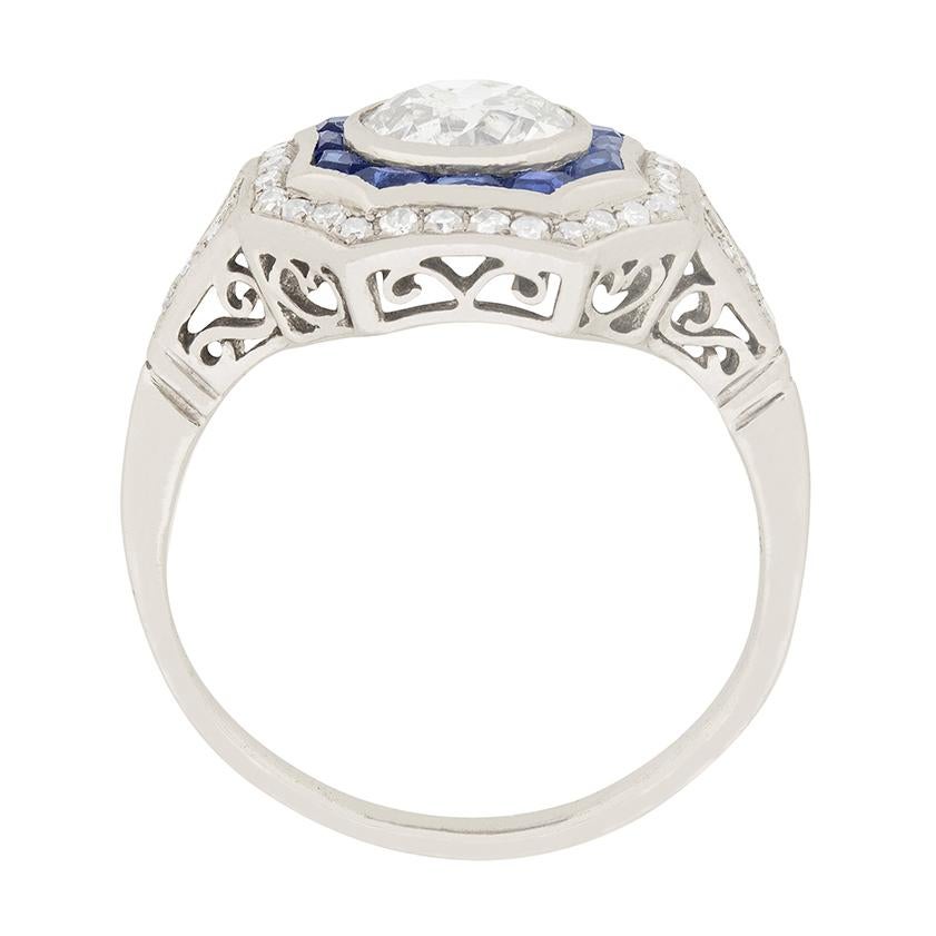 This stunning art deco ring showcases a 1.12 carat diamond surrounded by two halos of precious gems. The centre old cut diamond is an H colour and SI2 clarity. Surrounding the diamond is a halo of blue sapphires, totalling to 0.24 carat. The unique