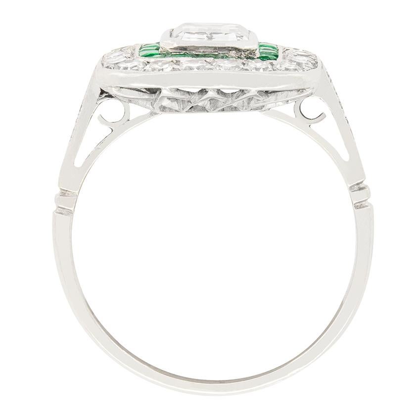 Dieser bezaubernde Art Deco Target Ring ist in der Mitte mit einem 1,15 Karat schweren Diamanten im Smaragdschliff besetzt. Er ist von einem Heiligenschein aus perfekt gefassten Smaragden von insgesamt 0,18 Karat umgeben. Ein weiterer Heiligenschein