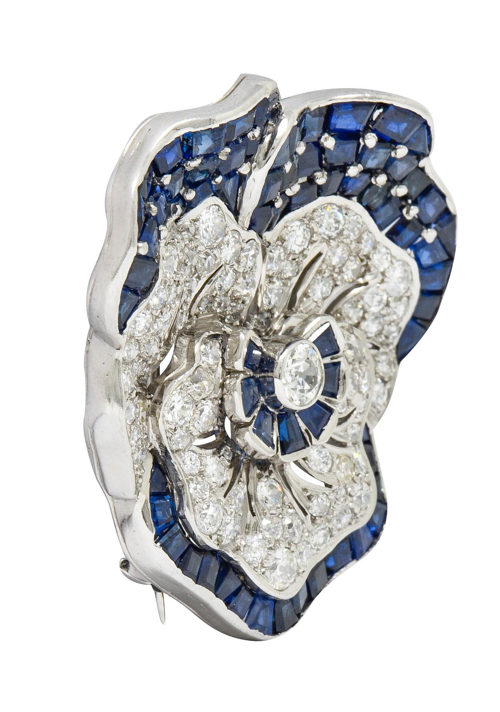 Flower brooch is designed as a dynamically petaled pansy

Centering a bezel set old European cut diamond weighing approximately 0.40 carat; K color with SI clarity

Surrounded by gemmed petals comprised of diamonds and sapphires

Total additional