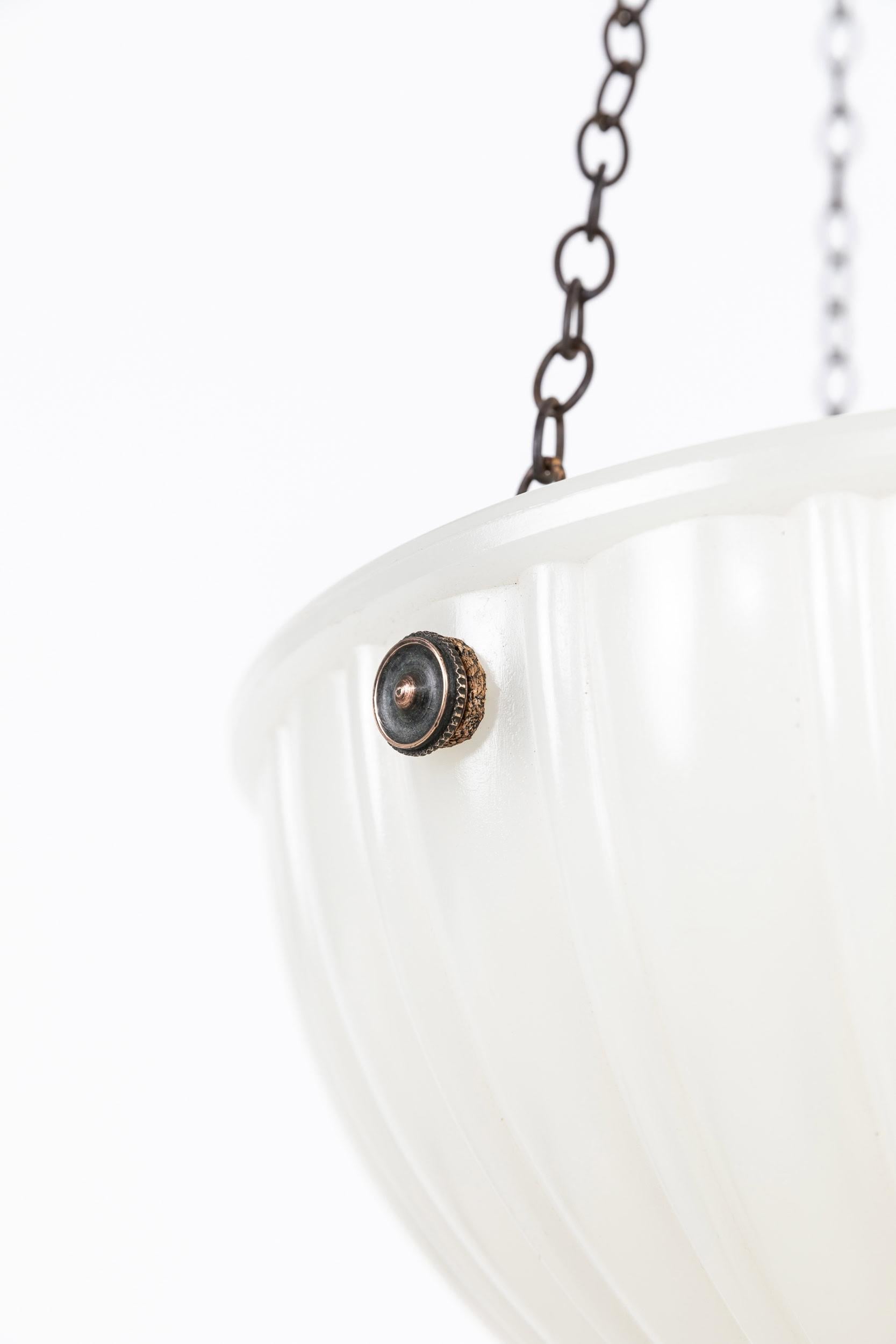 

A pressed glass moonstone plafonnier bowl pendant light. c.1930

Heavy duty pressed milk glass of fluted design, supported by integral hooks and ceiling plate. Chains could be shortened to suit drop.

Rewired with black twisted flex.
