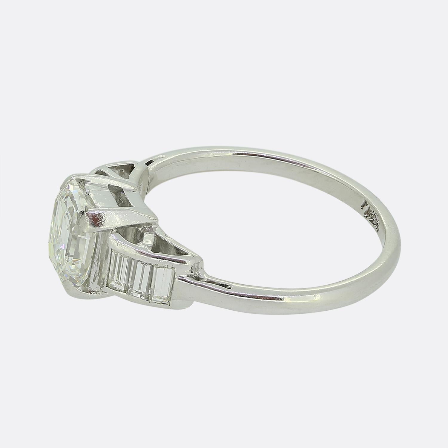 Here we have a delightful diamond ring exuding Art Deco elegance. This platinum piece plays host to a GIA certified 1.20 carat emerald cut diamond. This bright white principal stone sits proud at the centre of the face in a four clawed setting