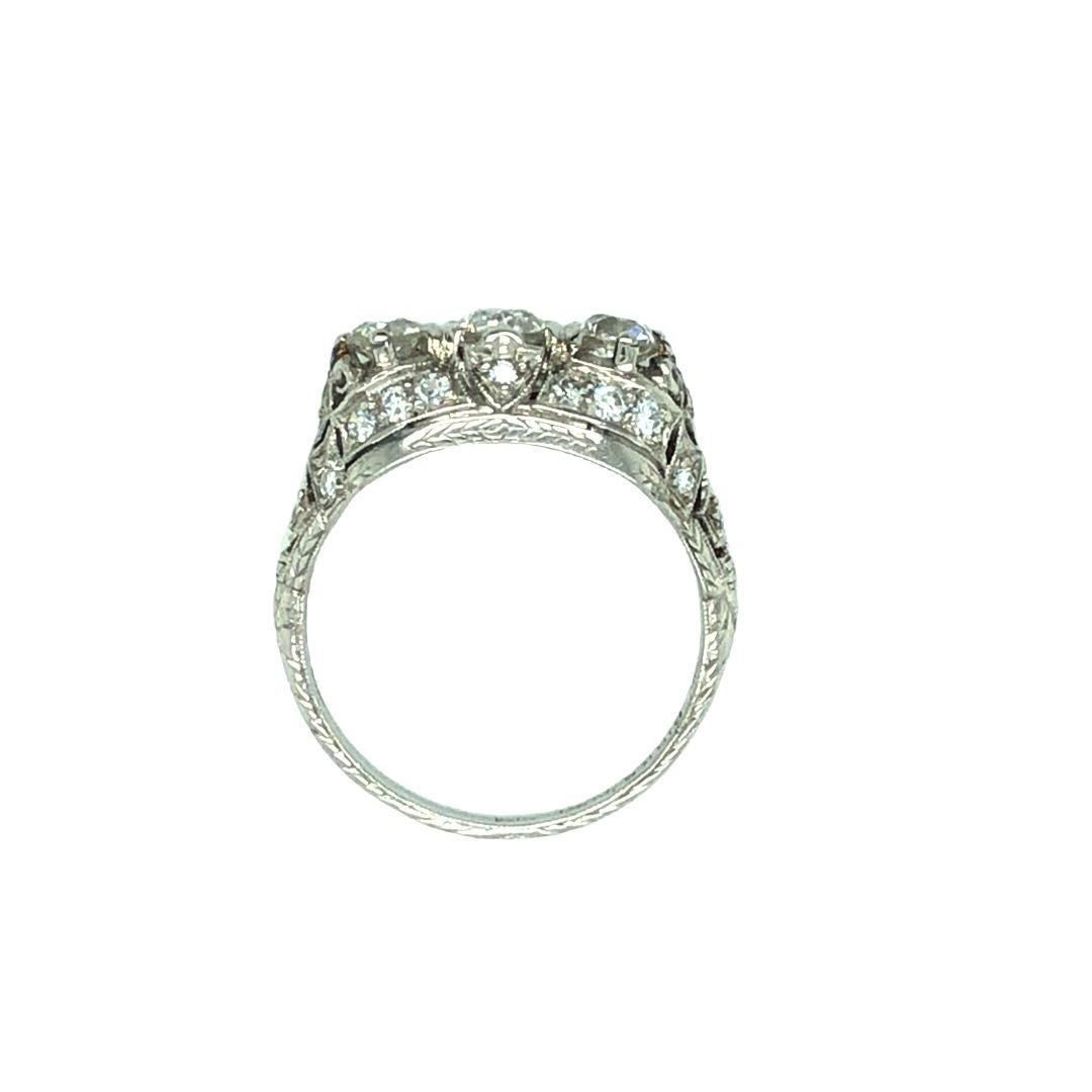 A sumptuous Art Deco diamond ring beautifully designed to highlight three white sparkling European diamonds in a richly detailed platinum and diamond mounting featuring milgrain, open work and a hand engraved shank. The three European cut diamonds