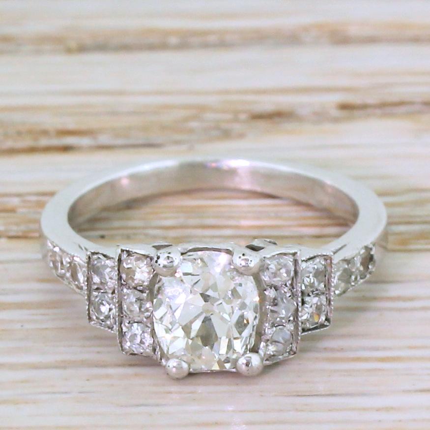 A ring that exudes the class and sophistication of the best Art Deco jewellery. The cushion shaped old mine cut diamond in the centre is white, bright and full of life. The stone is secured in a four-claw collet with ten (five either side) old cut