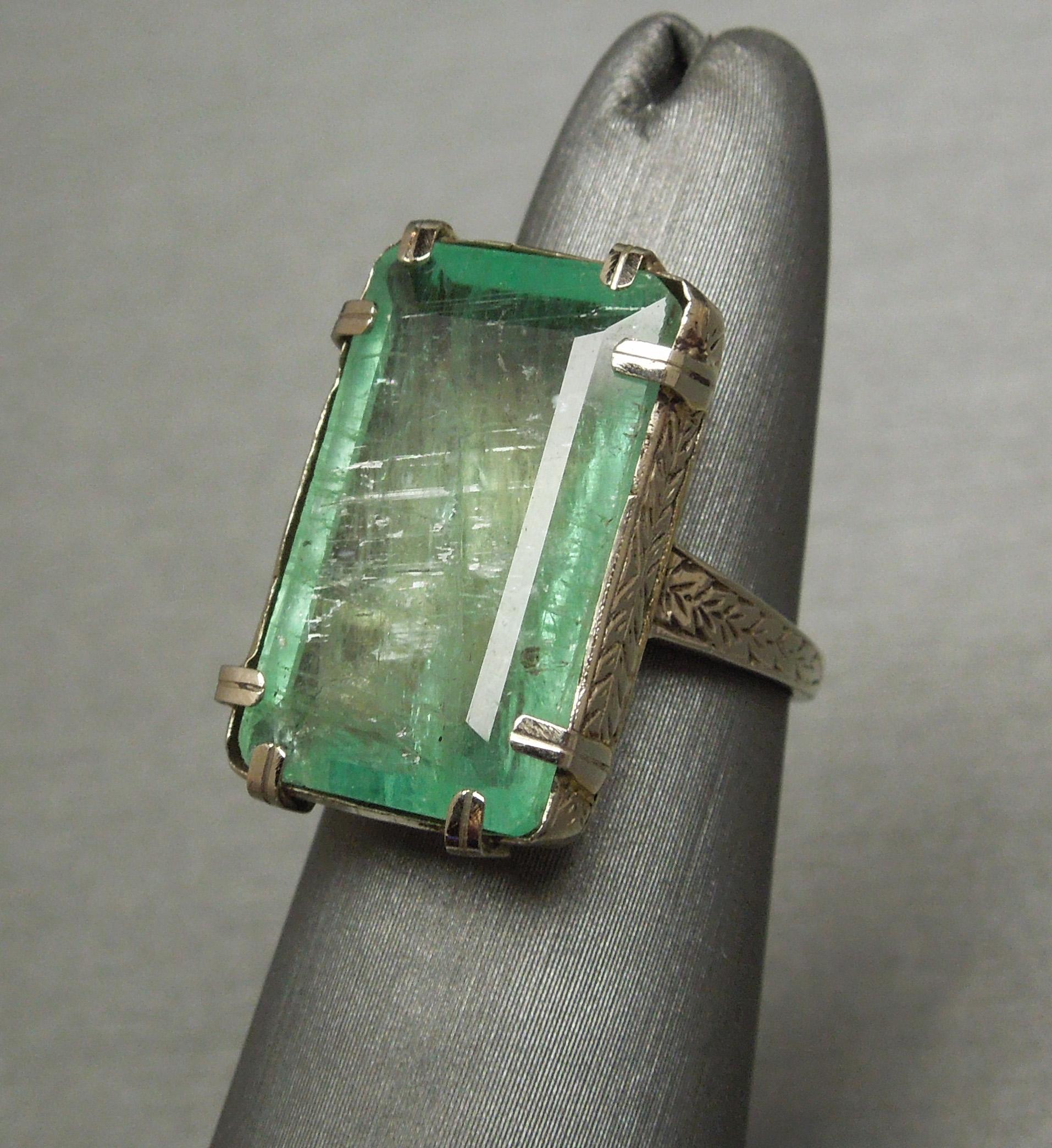 This True Art Deco Emerald Solitaire Ring features a single 12.50 carat Emerald cut Light Green Emerald, securely set in a Handmade 8-prong setting - (prongs typical of a 1920s Art Deco ring) .. Accented with Hand Engraving throughout. Very rare to