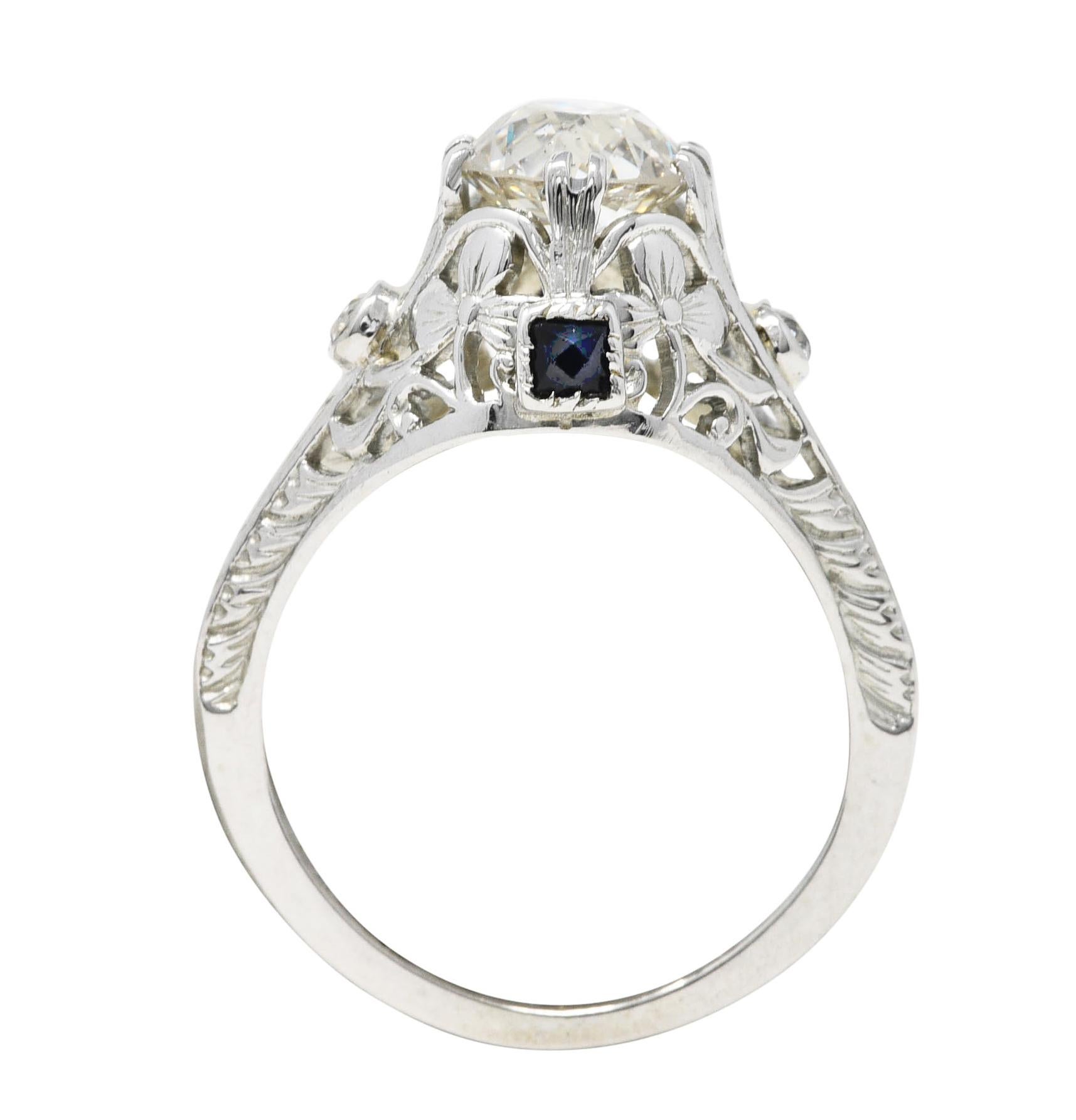 Featuring an old European cut diamond weighing approximately 1.20 carat - K color with SI2 clarity. Set by stylized split prongs in a pierced ornate mounting depicting scrolling florals at gallery. Accented by bezel set old European cut diamonds