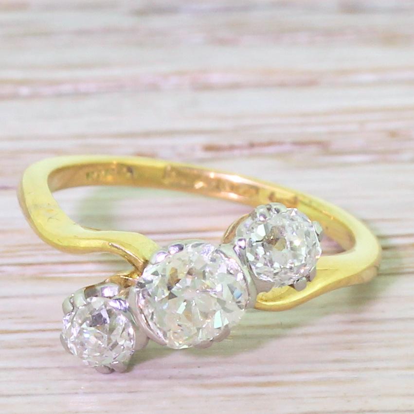 An utterly divine old cut diamond trilogy crossover ring. The central cushion shaped stone is laterally set, and flanked by a pair of round old cut diamonds – all set in platinum. All atop fine and beautifully shaped yellow gold band. A gorgeous