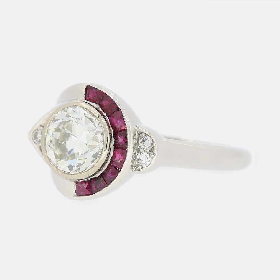 This is an Art Deco, French, ruby and diamond ring. The centre stone is a 1.30 carat transitional cut diamond that sits in a rubover mount. On one side of the diamond there are eight, rich red, calibrated rubies and on the other side a smaller