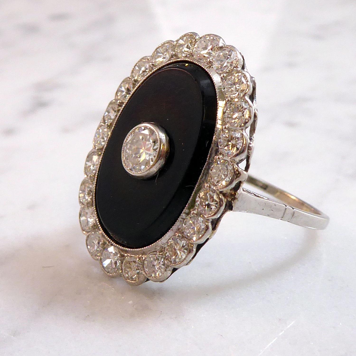 An Art Deco cluster ring in a stand out onyx and diamond combination.  The black onyx has been cut into an oval shape measuring 17.40mm long x 11.50mm wide x 1.80mm deep and weighs 1.97ct.  In a white metal millegrain setting to the centre of the