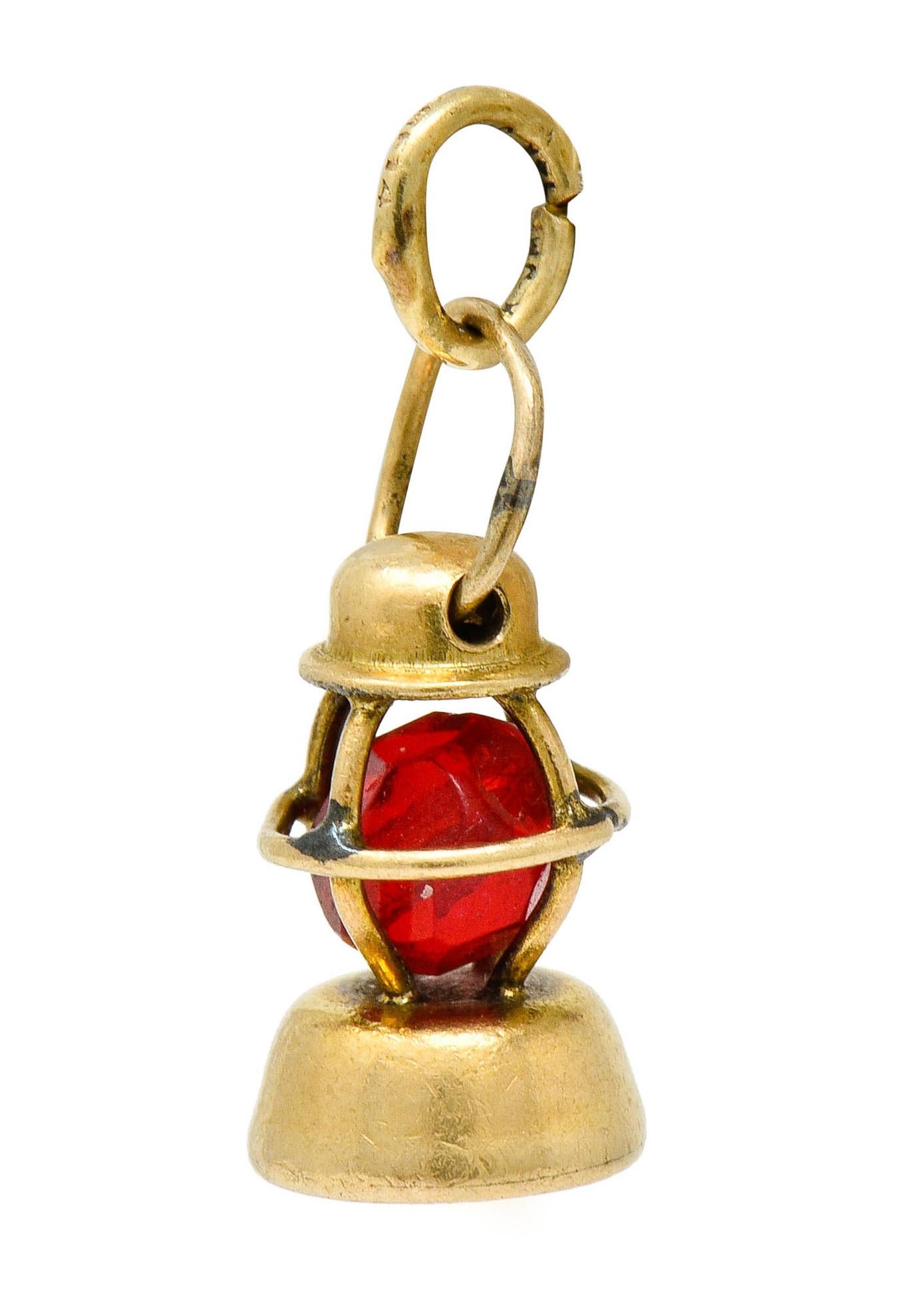 Designed as a nautical lantern with a polished gold top and base

With a gold wire cage surrounding a glowing red glass bead, insinuating a flame

Completed by a jump ring bale

With maker's mark for J.M. Fisher Company and stamped 14K for 14 karat