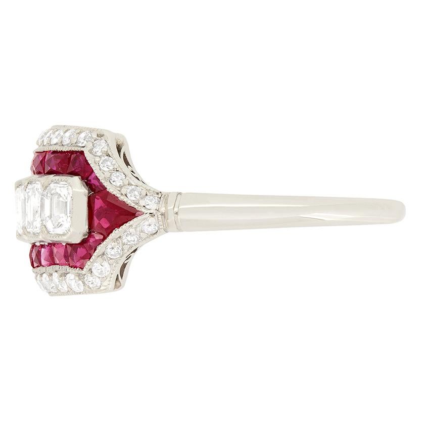 This showpiece cocktail ring comes to us from the Art Deco period. Seven, rub over set, 0.20 carat Emerald cut diamonds sit central to the ring with a halo of French cut rubies surrounding them. These rubies are expertly set and total 0.56 carat.