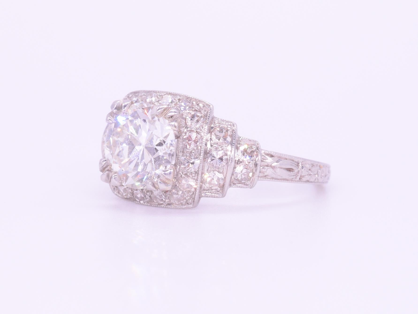 A transitional cut round diamond weighing approximately 1.40cts, of approximately H-I color and VS clarity, is set within a square stepped halo accented with single cut diamonds totaling approximately 0.50ct in a platinum mounting. Ring size