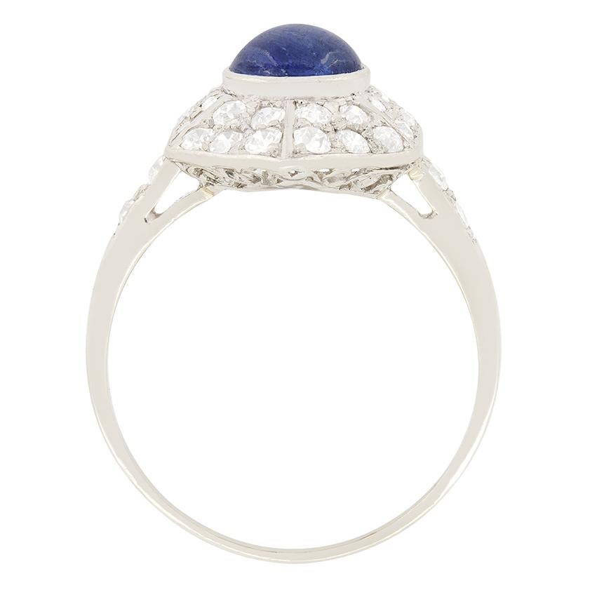 A captivating cluster ring dating back to the 1920's featuring a cabochon sapphire rub over set in the centre. The splendid sapphire weighs 1.45 carat and is surrounded by a geometrically shaped cluster of eight cut diamonds. In the cluster, there