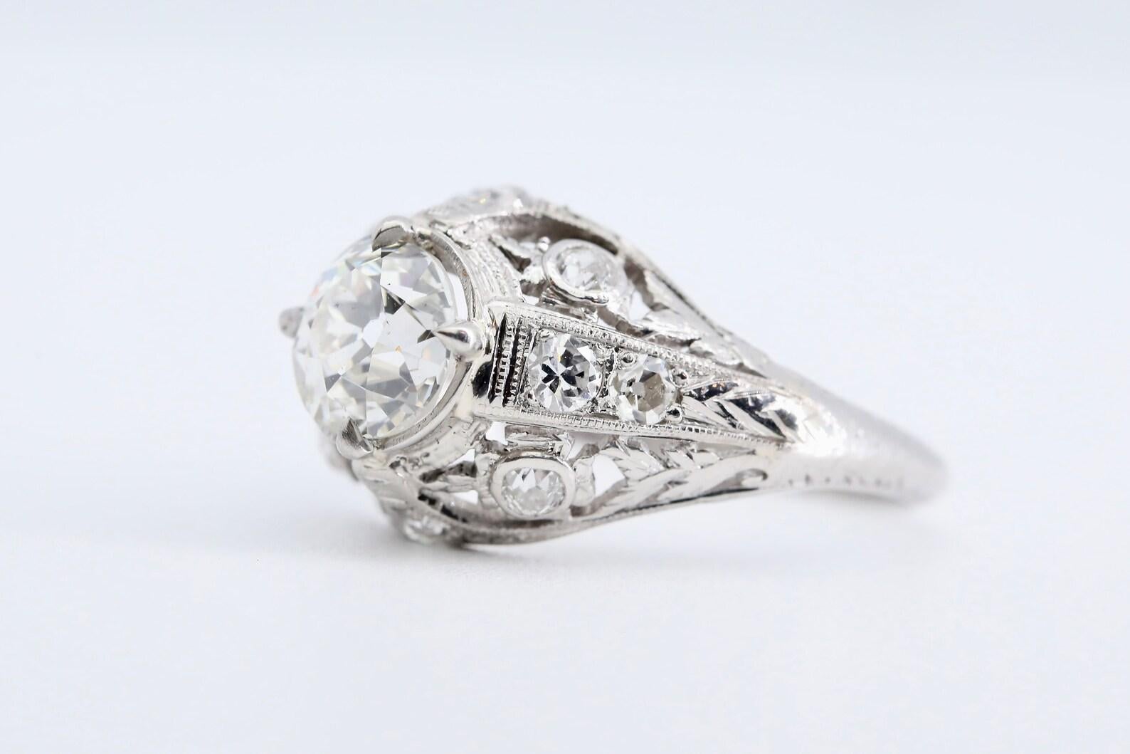 An Art Deco period floral motif diamond engagement ring crafted in platinum.

Centered by a 1.05 carat H color SI1 clarity old European cut diamond. 

Accented by hand engraved flowers, pierced filigree work, and a further 10 European cut diamonds