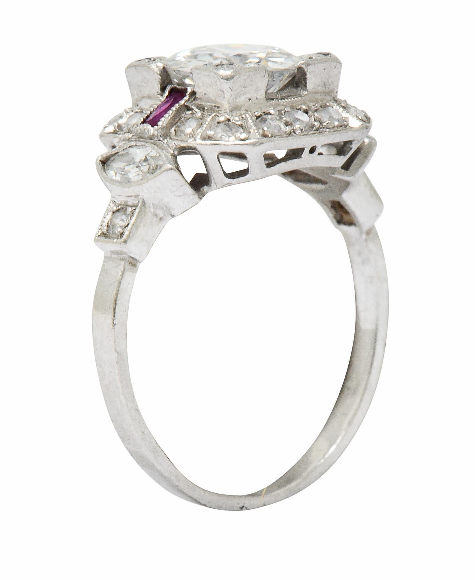Centering a transitional cut diamond weighing approximately 1.03 carats; H color with SI clarity

Set low in a square form head and flanked by two brightly colored and bezel set scissor cut rubies

With a single cut diamond halo and marquise cut