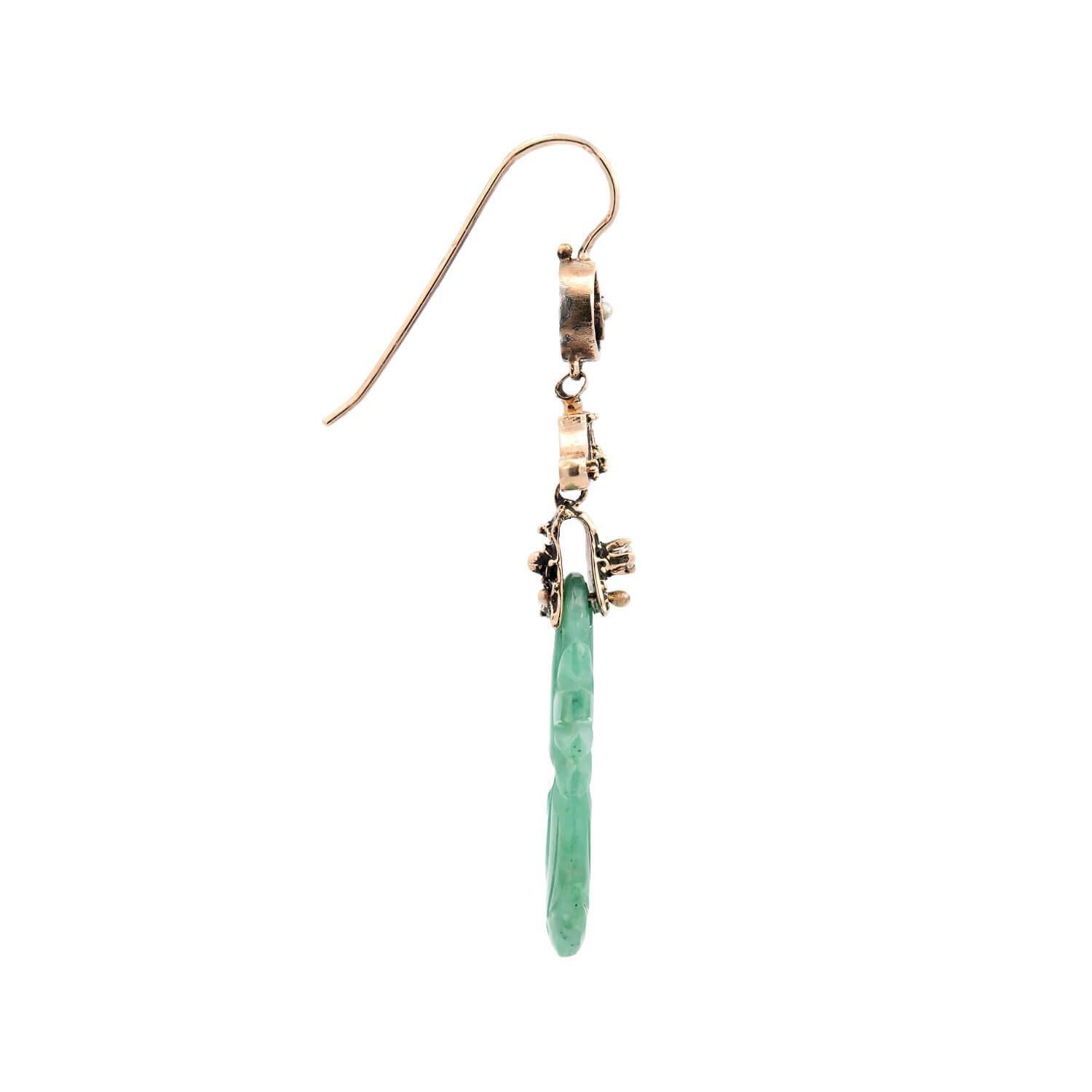 A beautiful pair of carved jade earrings from the Art Deco (ca1920s) era! Crafted in 14k yellow gold, each earring begins with a circular surmount. The center of each surmount features a small pearl, which rests within a starburst-shaped frame.
