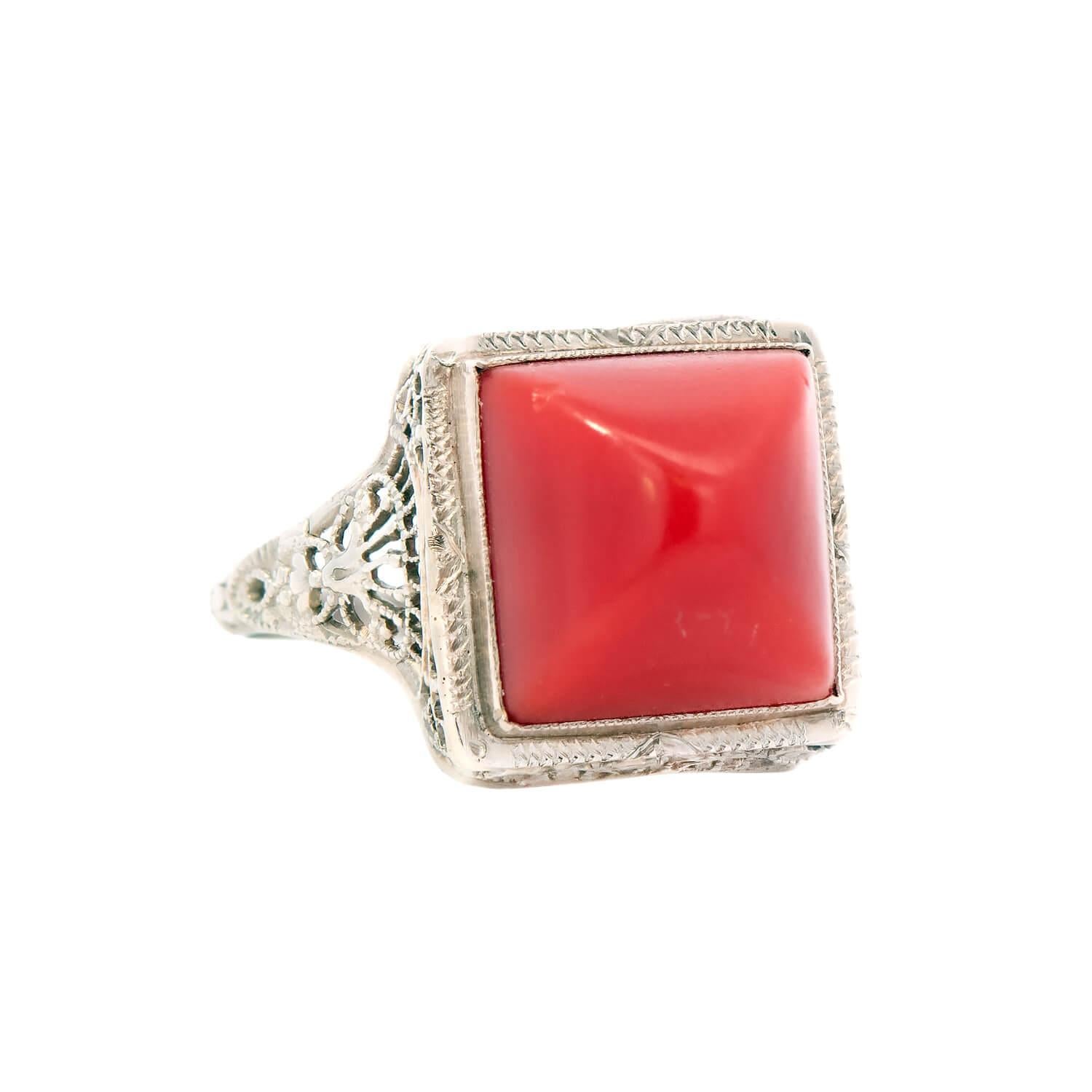 Une fabuleuse bague en corail de l'époque Art Déco (ca1920) ! Réalisée en or blanc 14k, la bague présente un cabochon central en corail, retenu par un chaton en milgrain. Le corail repose dans un cadre de forme carrée, décoré de subtiles gravures.