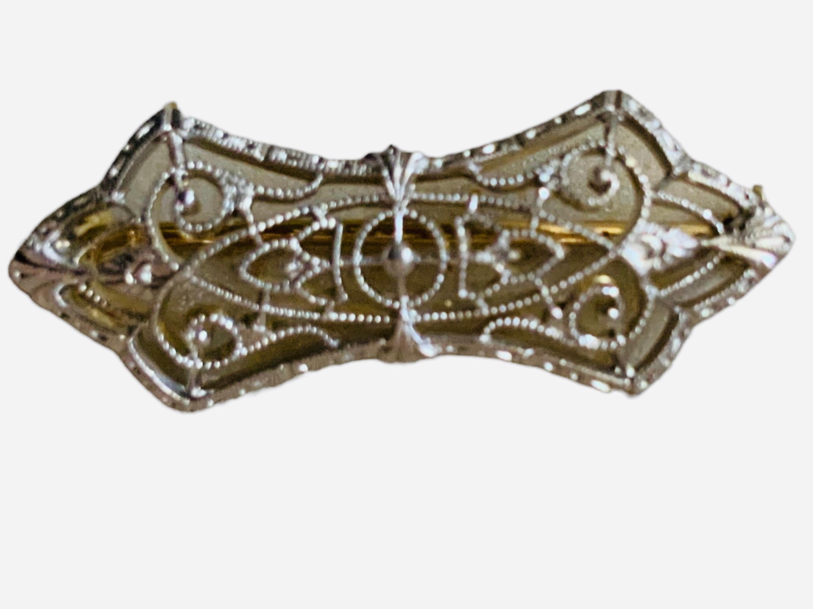 This is a 14K Gold Filigree Small Pin. It depicts an Art Deco engraved white and yellow gold bow like shaped pin. It is made of filigree with tiny leaves, hearts and scrolls. The pin has a safety C- clasp in the back and is also hallmarked 14K in