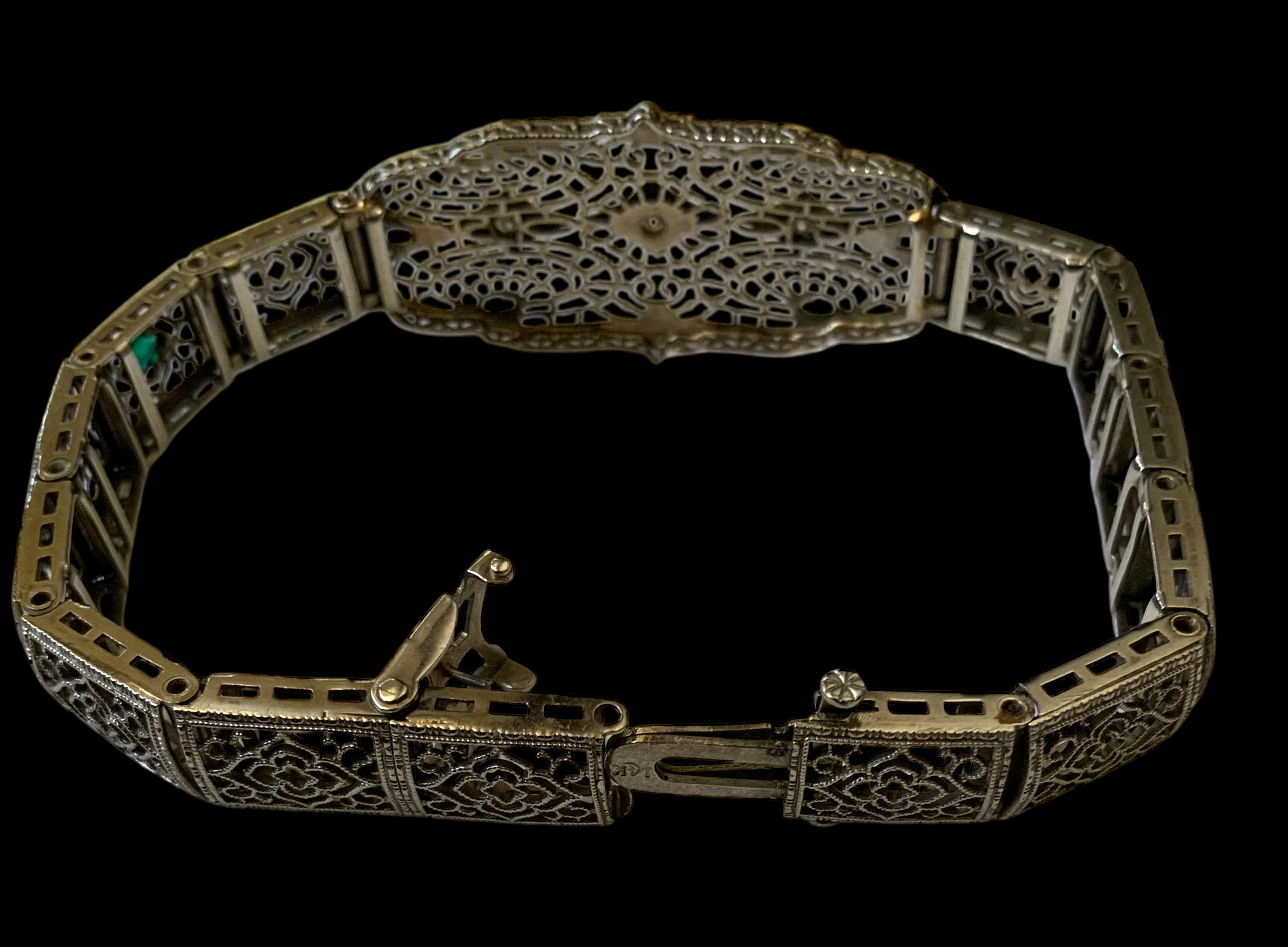 This an Art Deco 14K White Gold Diamond Bracelet. It depicts a link bracelet adorned with a filigree open work pattern of four elongated ovals decorated with crowns like in the center and flowers in its rectangular links. Three single cut diamonds