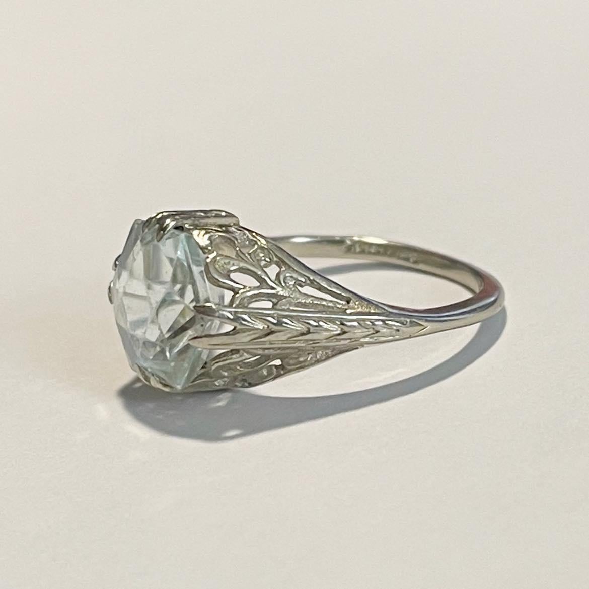This unique blossom is a stunner. Crafted in 14K white gold the open filigree work of the mount matches perfectly with the hexagonal cut of the sky blue aquamarine. The shape of this gem is unique and beautiful. Rising in popularity in the Art Deco