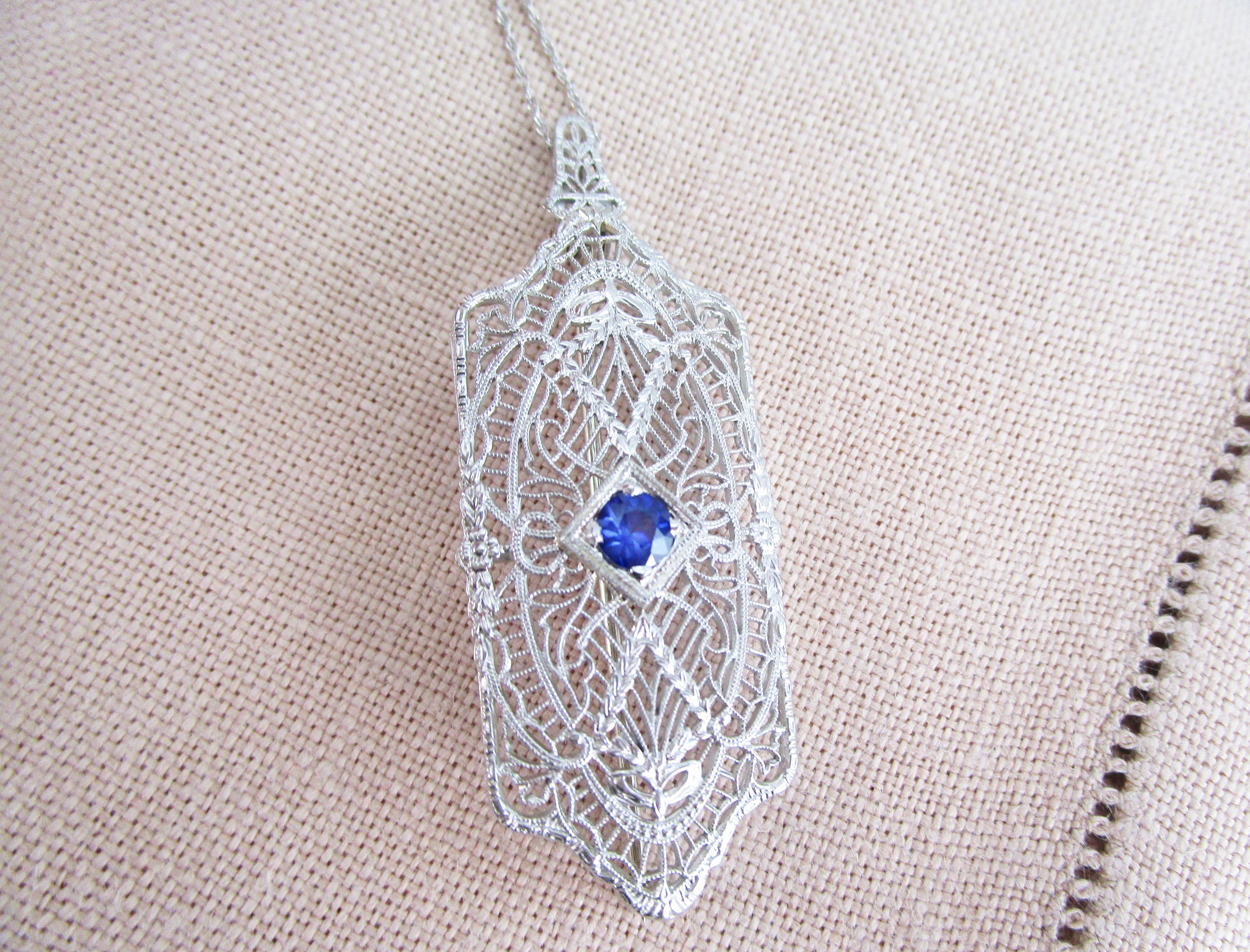 This is an enchanting Art Deco pin pendant in 14k white gold with beautiful filigree work and a breathtakingly blue sapphire in the center. The delicate filigree creates a lace-like look that makes this pin pendant delicate, but incredibly elegant!