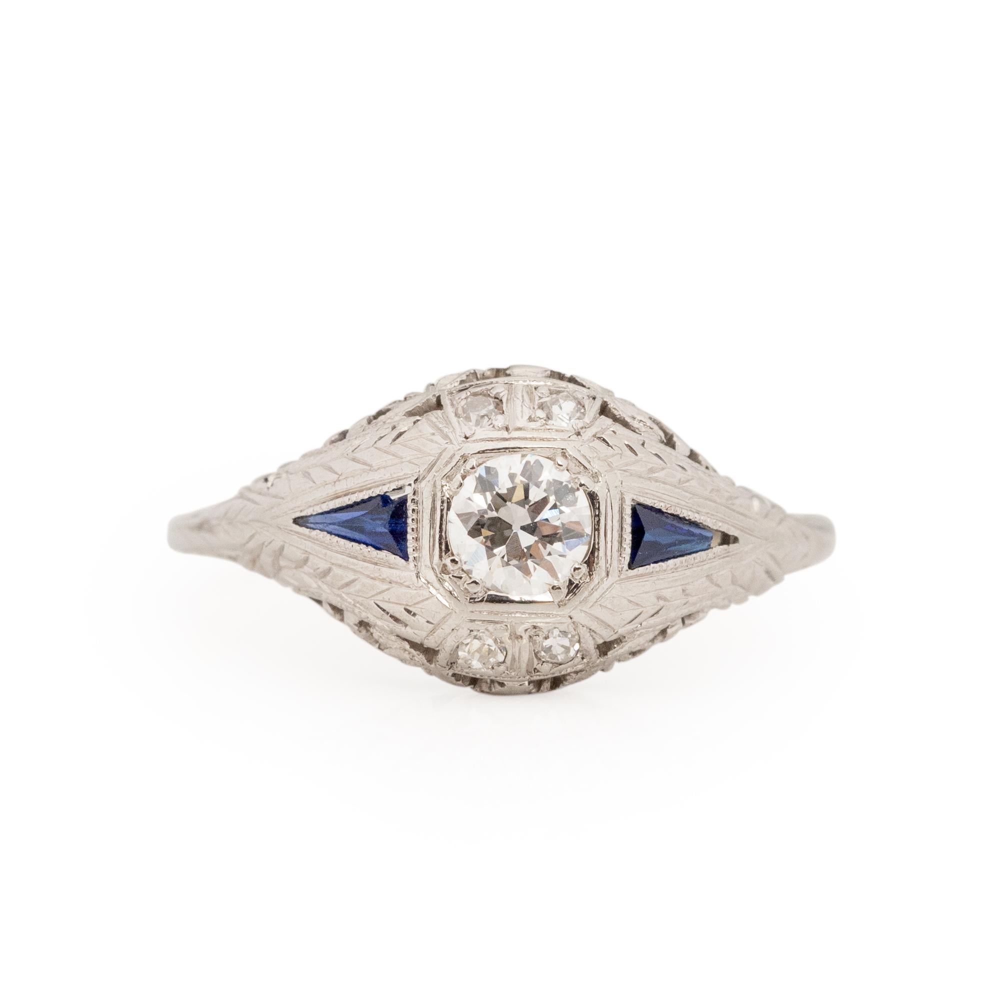 This little art deco classic has beautiful filigree carving along the gallery that allows light through. Lighting the center diamond and accent sapphires from underneath. The floral filigree design is a wonderful compliment to the white gold that