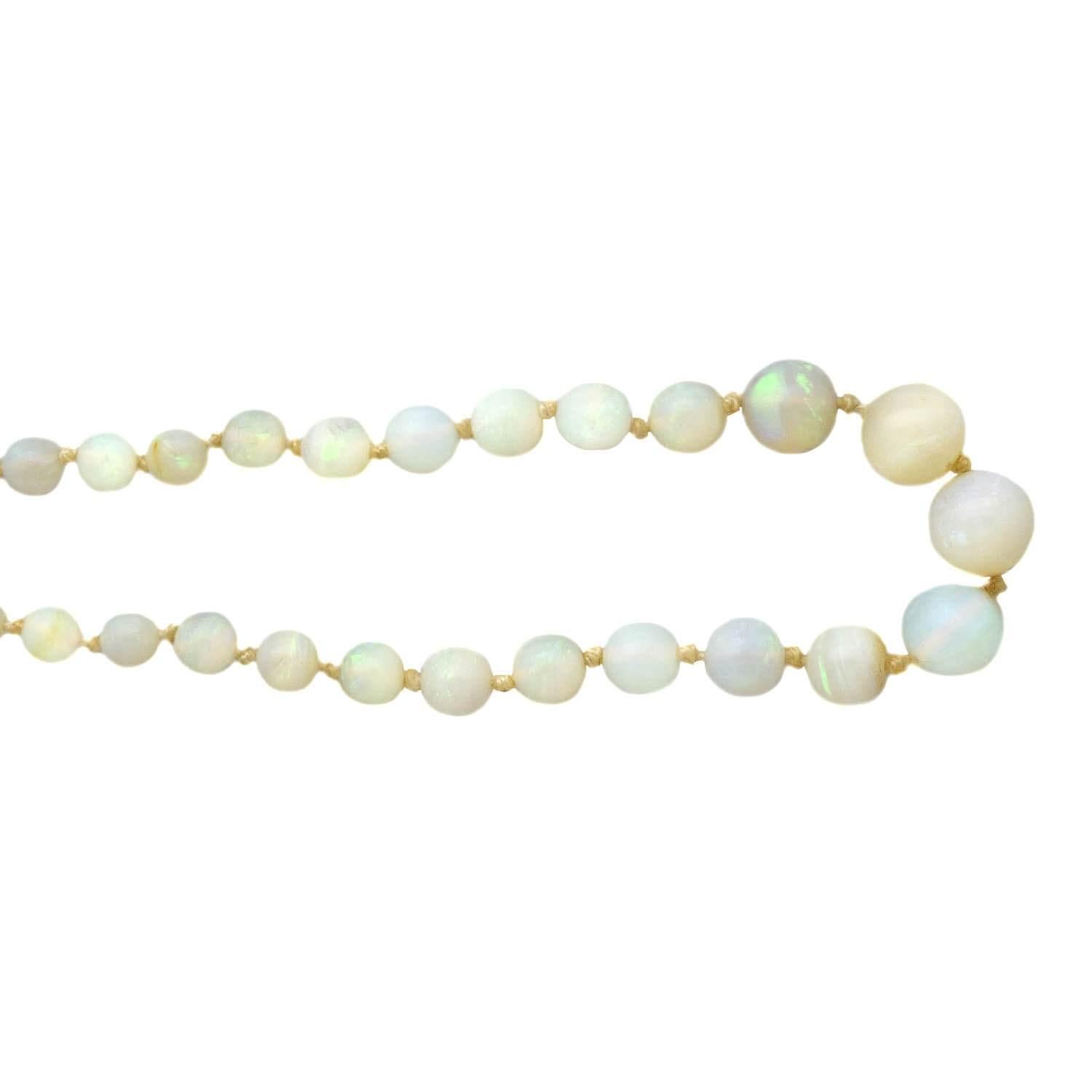 A lovely white opal necklace from the Art Deco (ca1930s) era! Graduated white opals flash a wonderful rainbow of color, knotted between white silk cord. The beads are translucent and their nearly-neon hues truly glow from within. The necklace is
