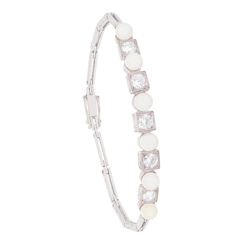Ce bracelet art déco présente une rangée de perles alternant avec des diamants taille transition. Les cinq diamants totalisent 1,50 carat, sont de couleur G et de pureté VS2. Les diamants sont sertis dans des montures de forme carrée, qui