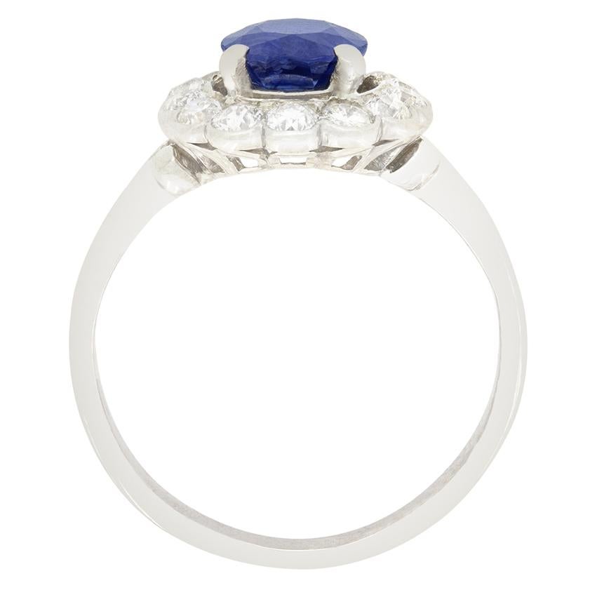 Risalente agli anni '20, questo splendido anello a grappolo presenta uno zaffiro naturale al centro. Lo zaffiro dal taglio ovale pesa 1,50 carati ed è incastonato in un'aureola di diamanti taglio vecchio. Questi diamanti hanno un peso complessivo di