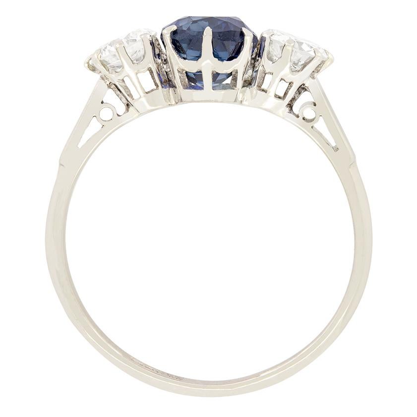 This beautiful Art Deco trilogy ring is set with a lovely 1.50 carat Sapphire at its centre, with two 0.40 carat transitional cut diamonds flanking. The central sapphire is an entirely natural, cushion cut stone. Both diamonds match in quality at G