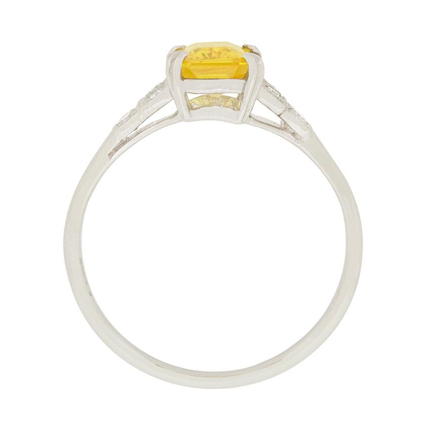 A vibrant 1.50 carat yellow sapphire is the star of this art deco ring. The emerald cut sapphire is flanked by 0.18 carat of eight cut diamonds, with three on each shoulder. They are great quality, with grades of F colour and VS clarity. The