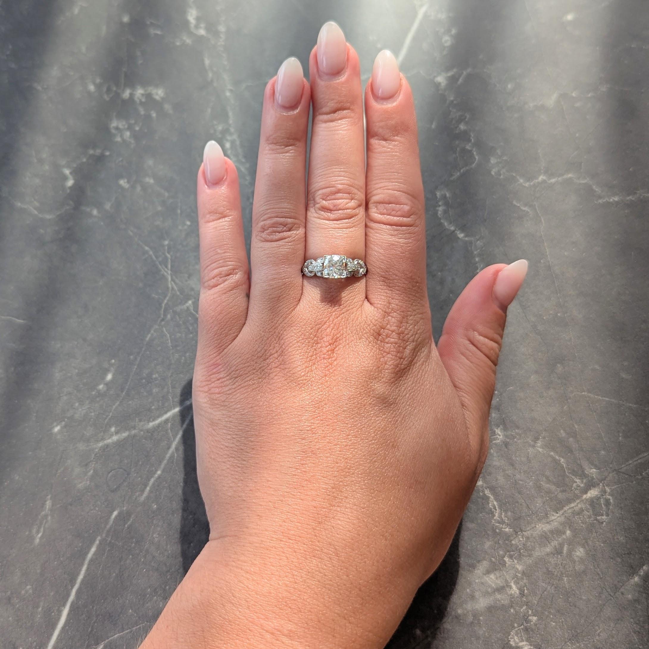 Centering an old mine cut diamond weighing approximately 1.20 carats - I color with VS2 clarity
Bead set in a square form head and flanked by pierced buckle motif shoulders
Bead set throughout with single cut diamonds throughout
Weighing