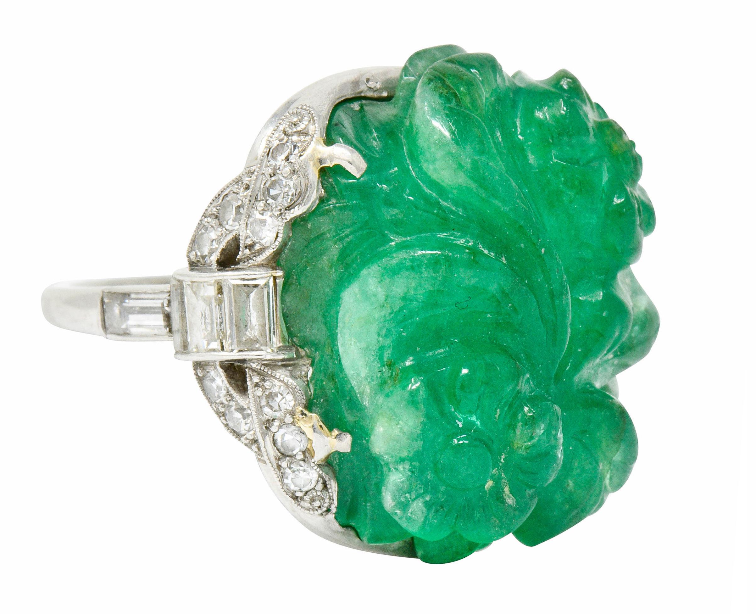 Centering a bright green Colombian emerald weighing approximately 15.00 carats

Deeply hand carved to depict a flourishing floral and foliate motif

Prong set in an ornately scalloped mounting accented by single and baguette cut diamonds, weighing