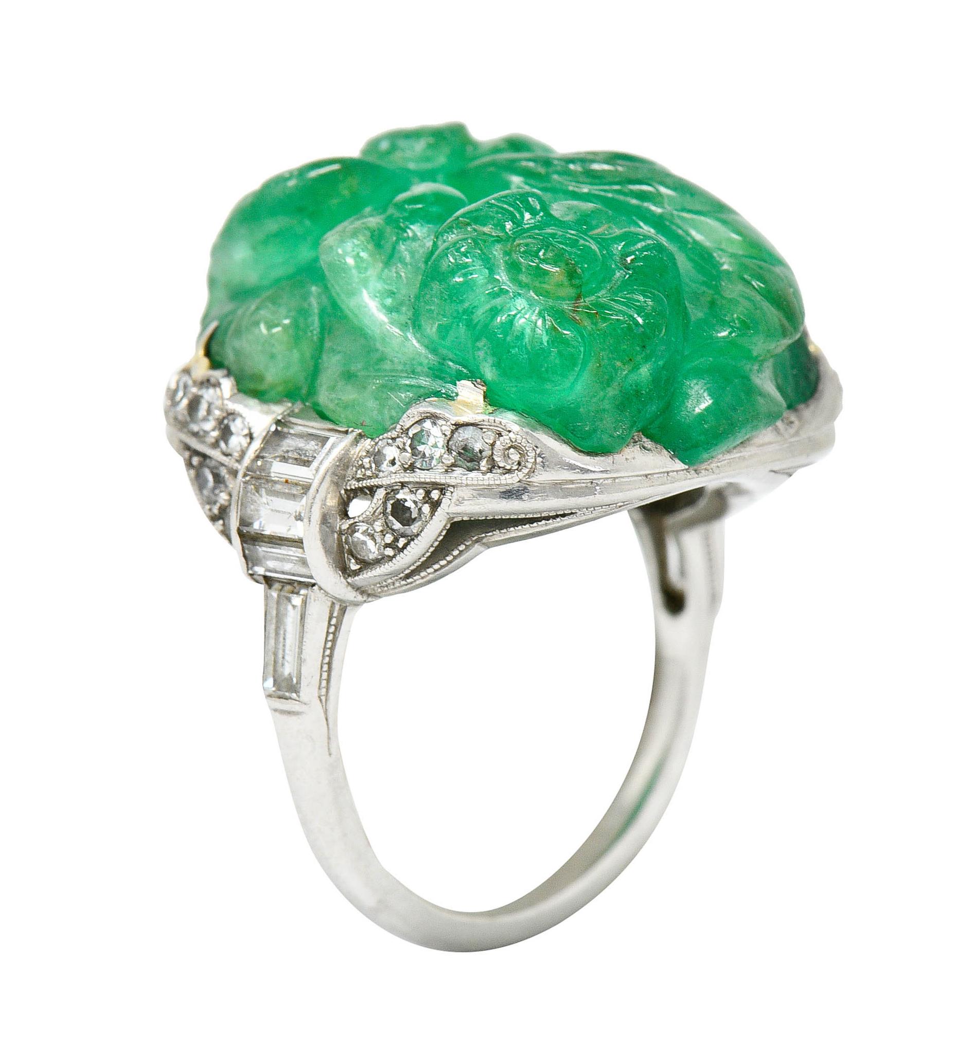 Centering a bright green Colombian emerald weighing approximately 15.00 carats

Deeply hand carved to depict a flourishing floral and foliate motif

Prong set in an ornately scalloped mounting accented by single and baguette cut diamonds, weighing