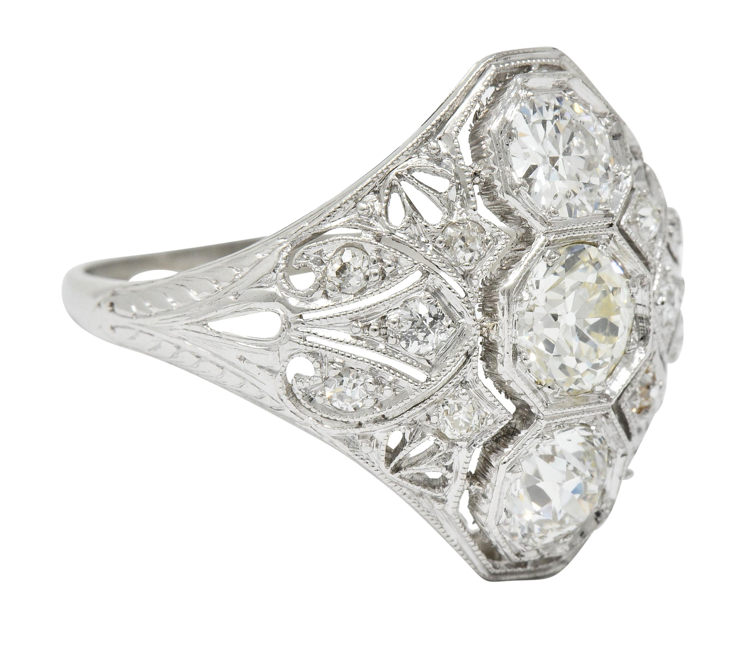 Dinner style ring with pierced details, milgrain edges, and engraved foliate shoulders

Centering three old European cut diamonds weighing in total approximately 1.35 carats

Set low in hexagonal heads, North to South, with I to K color and VS in