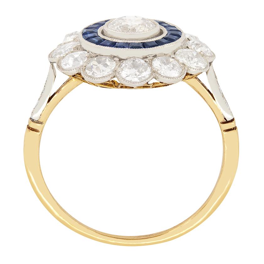 A 0.40 carat old cut diamond is set within a ring of deep blue sapphires in this beautiful target ring from the art deco period. The surrounding sapphires are baguette cut stones totalling 0.54 carat. A further ring of diamonds, totalling 1.20