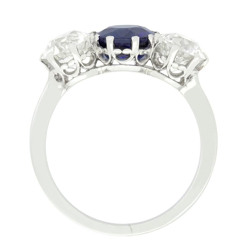 Un saphir bleu intense est placé entre deux diamants brillants de taille ancienne dans cette bague trilogie Art déco. Le saphir pèse 1,65 carat et est naturel et non chauffé. Les diamants de taille ancienne pèsent 1,00 carat chacun et sont d'une