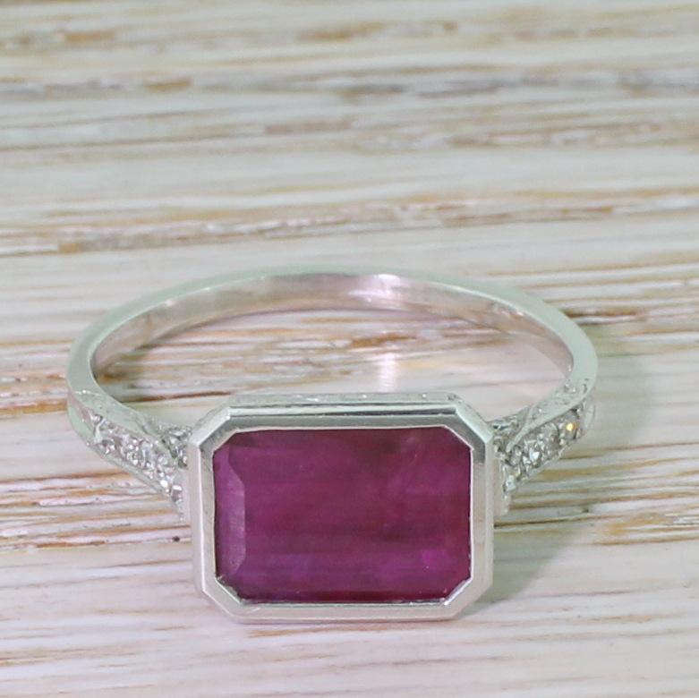 Such an exciting ring. The natural and unheated emerald cut ruby displays a deep purplish red and is set laterally in a rubover platinum setting. The ruby is cut shallow to allow plenty of light to pass through the stone, as well as giving it a