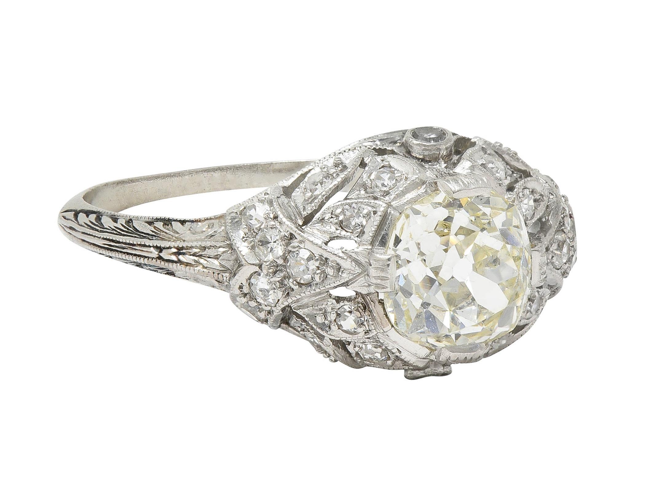 Centering an old mine cut diamond weighing 1.40 carats - M color with SI1 clarity
Set with engraved wide prongs with a pierced foliate motif bombé surround
Bead and bezel set with old single cut diamonds throughout 
Weighing approximately 0.36 carat