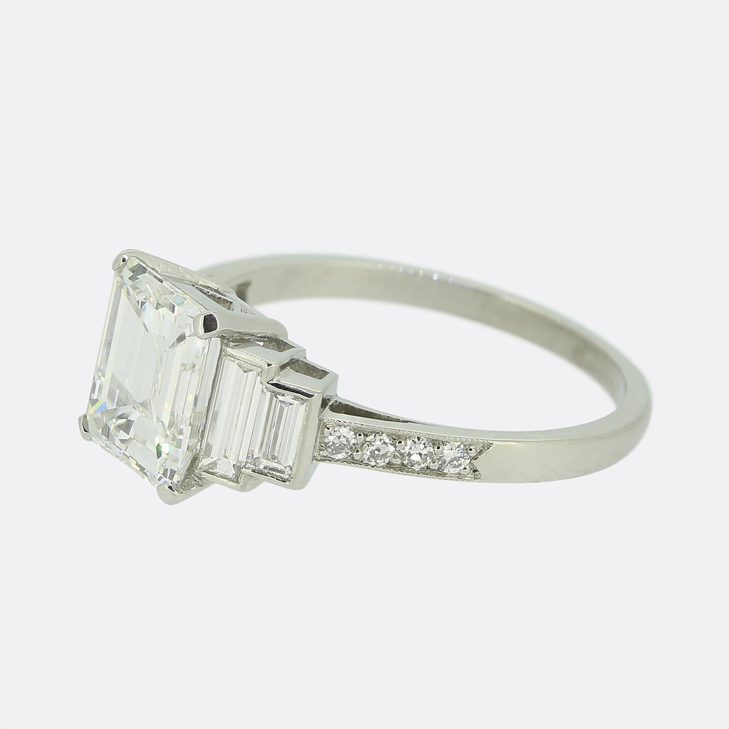 Here we have an exquisite Art Deco engagement ring. This piece features a stunning emerald-cut white diamond as the centre stone, complemented by brilliant-cut white diamond accents. Crafted in luxurious platinum, the ring showcases the geometric