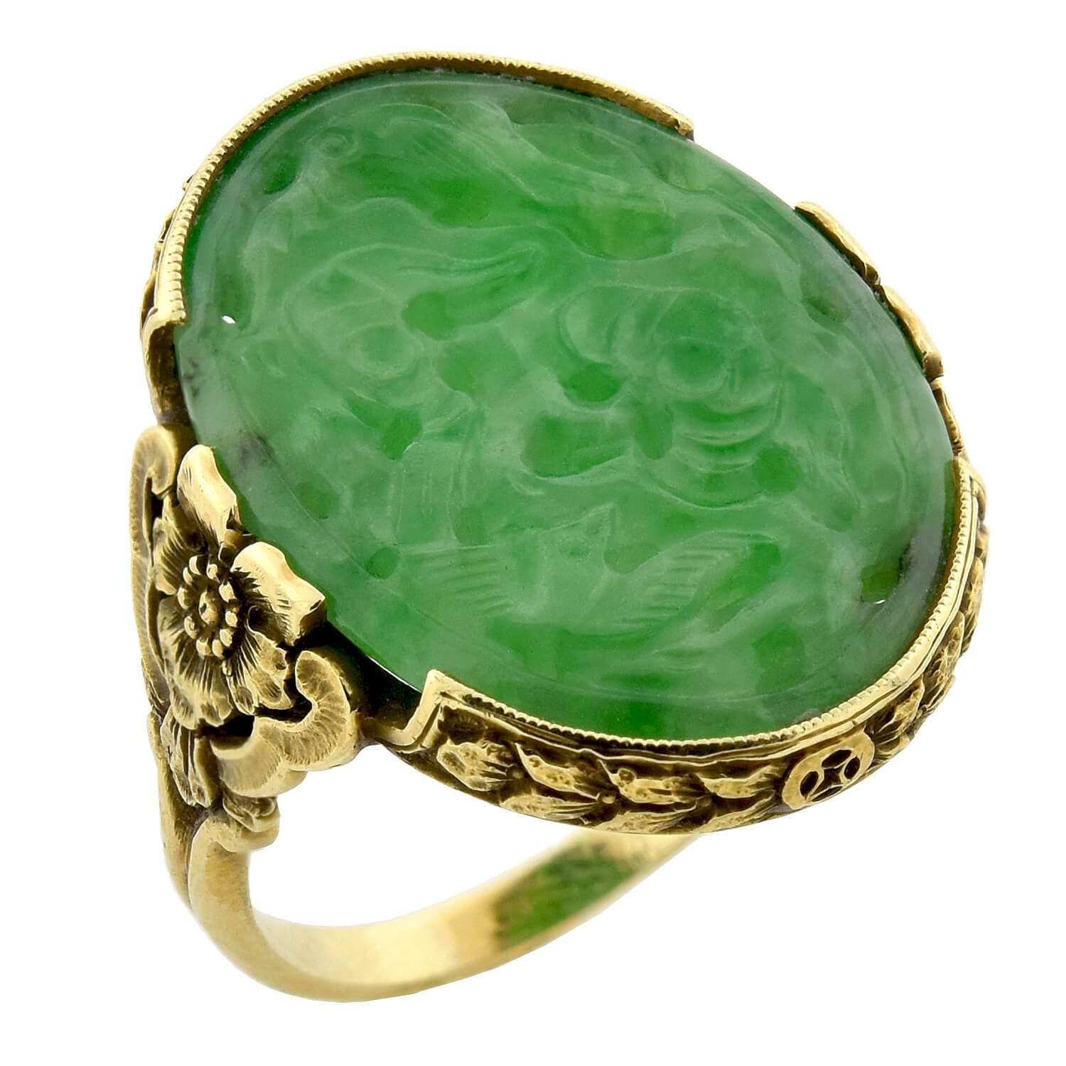 A stunning jadeite ring from the Art Deco (ca1920s) era! This beautiful piece is crafted in vibrant 18kt yellow gold and features an artistic oval-shaped jadeite plaque resting in the center of a decorative floral mounting. The natural, untreated