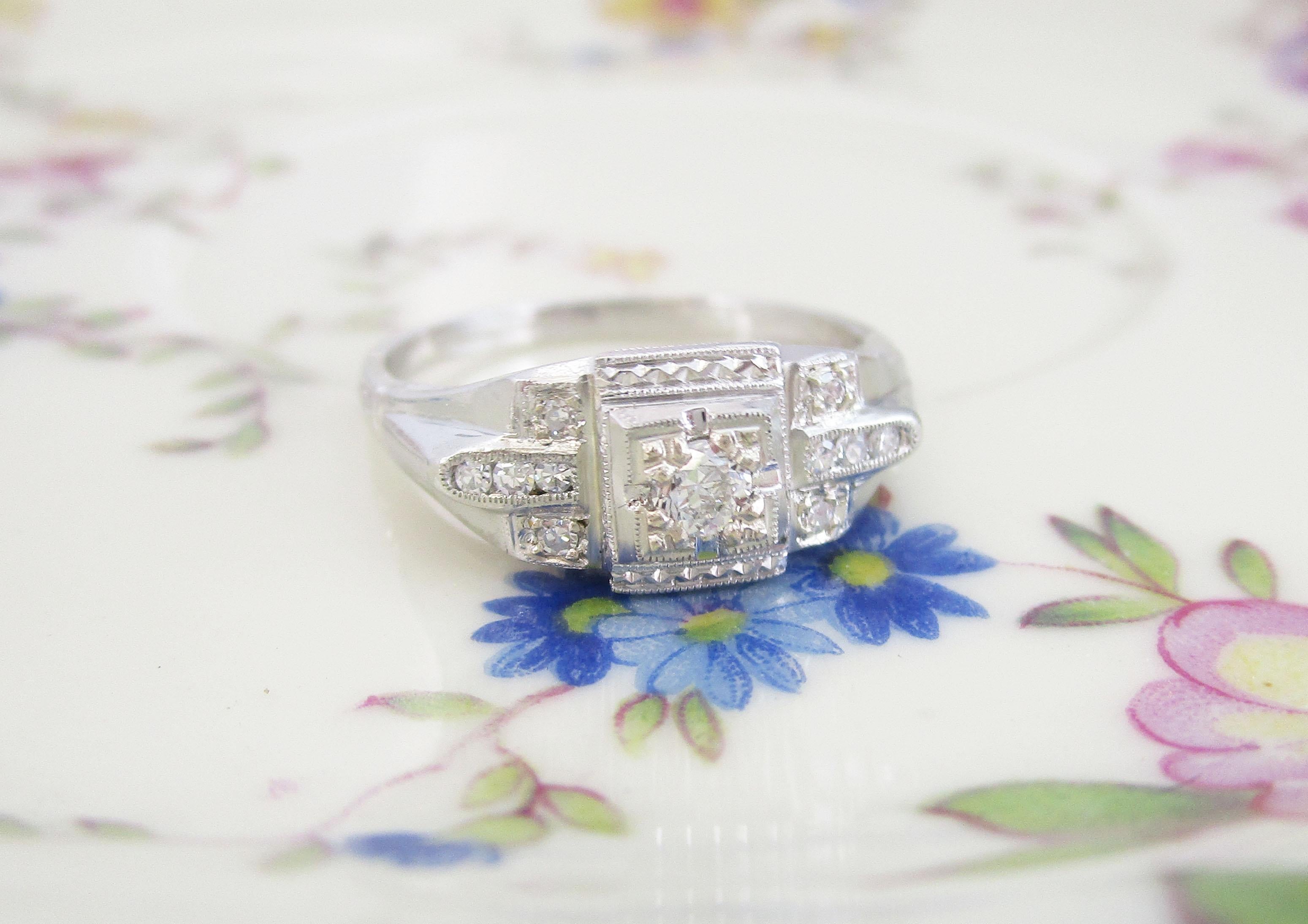 This beautiful Art Deco engagement ring is in 18k white gold and has a beautiful old euro cut diamond center. The diamond center is accented by ten smaller sparkling diamonds surrounded with milgrain details. The Art Deco influence is clear in the