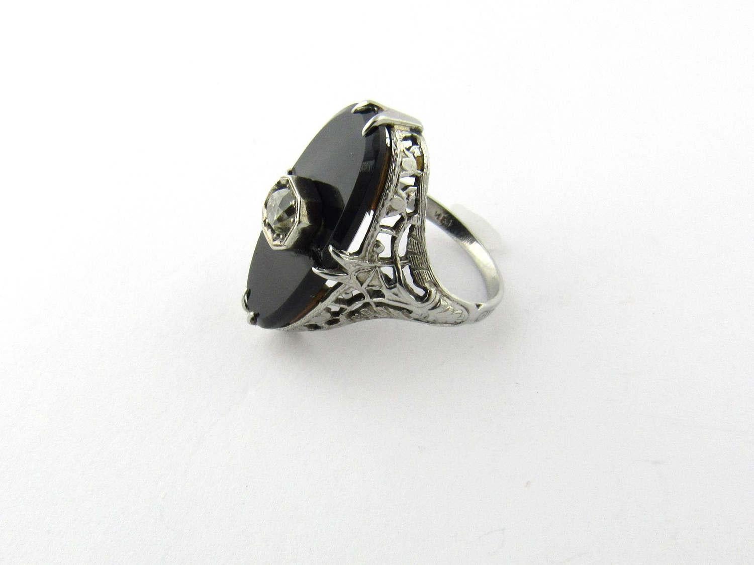 Vintage Art Deco 18 Karat White Gold Onyx and Diamond Ring- 

This lovely ring features an oval black onyx stone measuring 21 mm x 11 mm. A sparkling old mine cut diamond is set in its center. Approximate diamond weight: .25 ct. Color: L-M, Clarity: