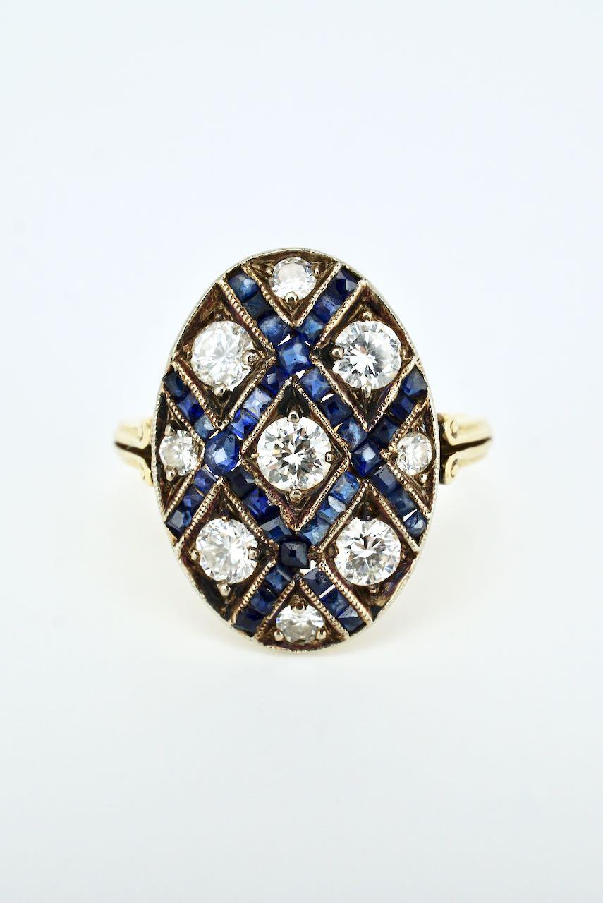 An Art Deco dress ring featuring an oval table bead set with 9 round brilliant cut diamonds within a channel set lattice of blue sapphires on a fine tapered shank with a split scroll motif to the shoulders - a beautifully detailed Art Deco dress