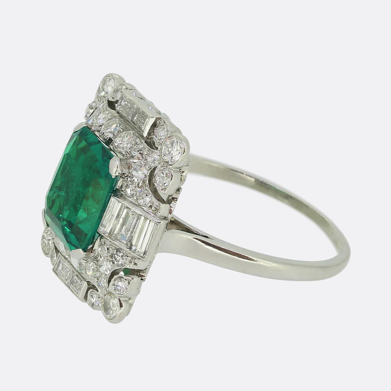 Here we have an outstanding platinum Art Deco cluster ring showcasing a striking emerald-cut green emerald of Colombian origin at its centre. Surrounding this vibrant principal stone is a dazzling array of bright white straight baguette cut diamonds