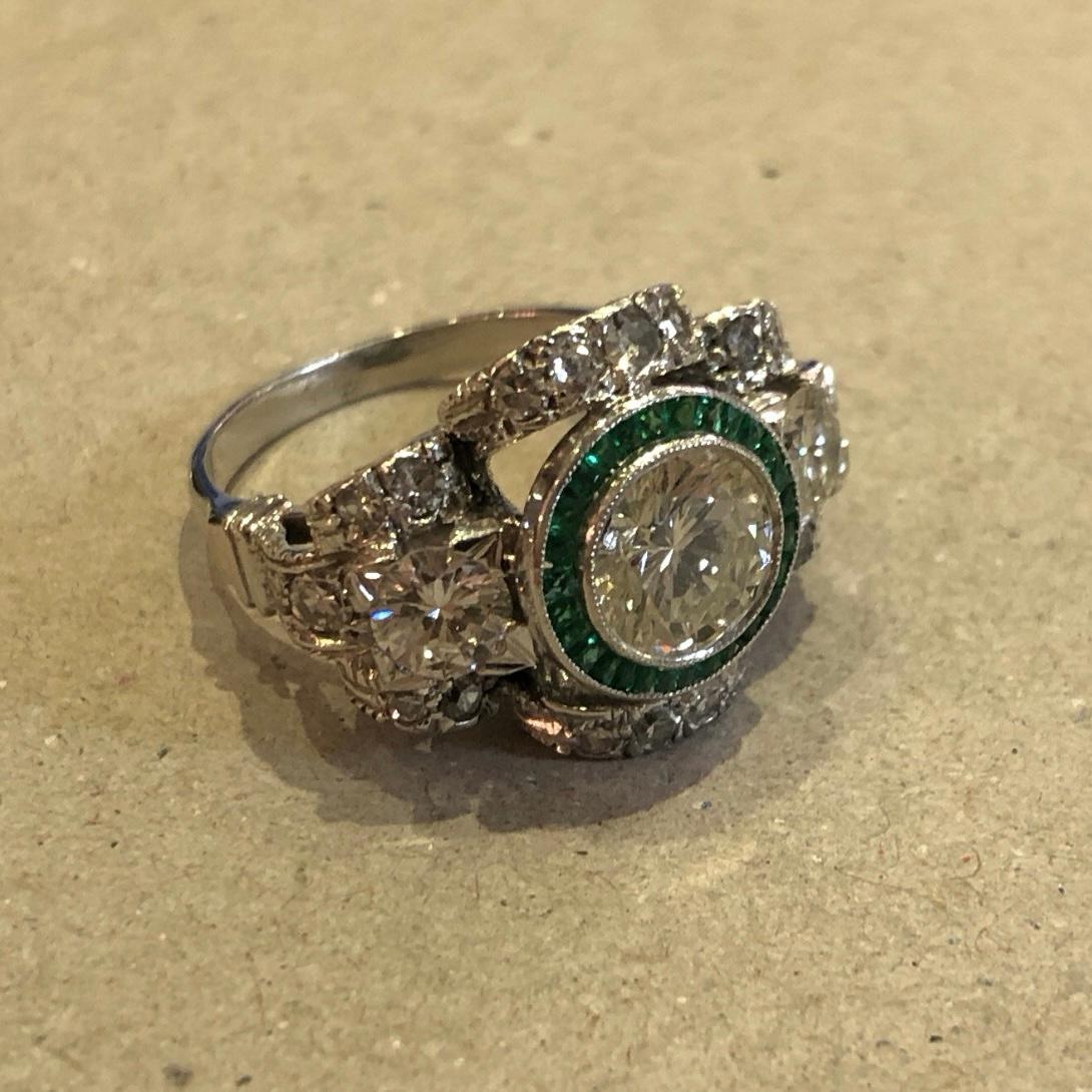 A 20th Century Diamond and Emerald Target Cocktail Ring. This spectacular ring designed in a style which is iconically Art Deco features a Transitional round brilliant-cut diamond millegrain-set to the centre, encircled by a halo of 28 similarly-set
