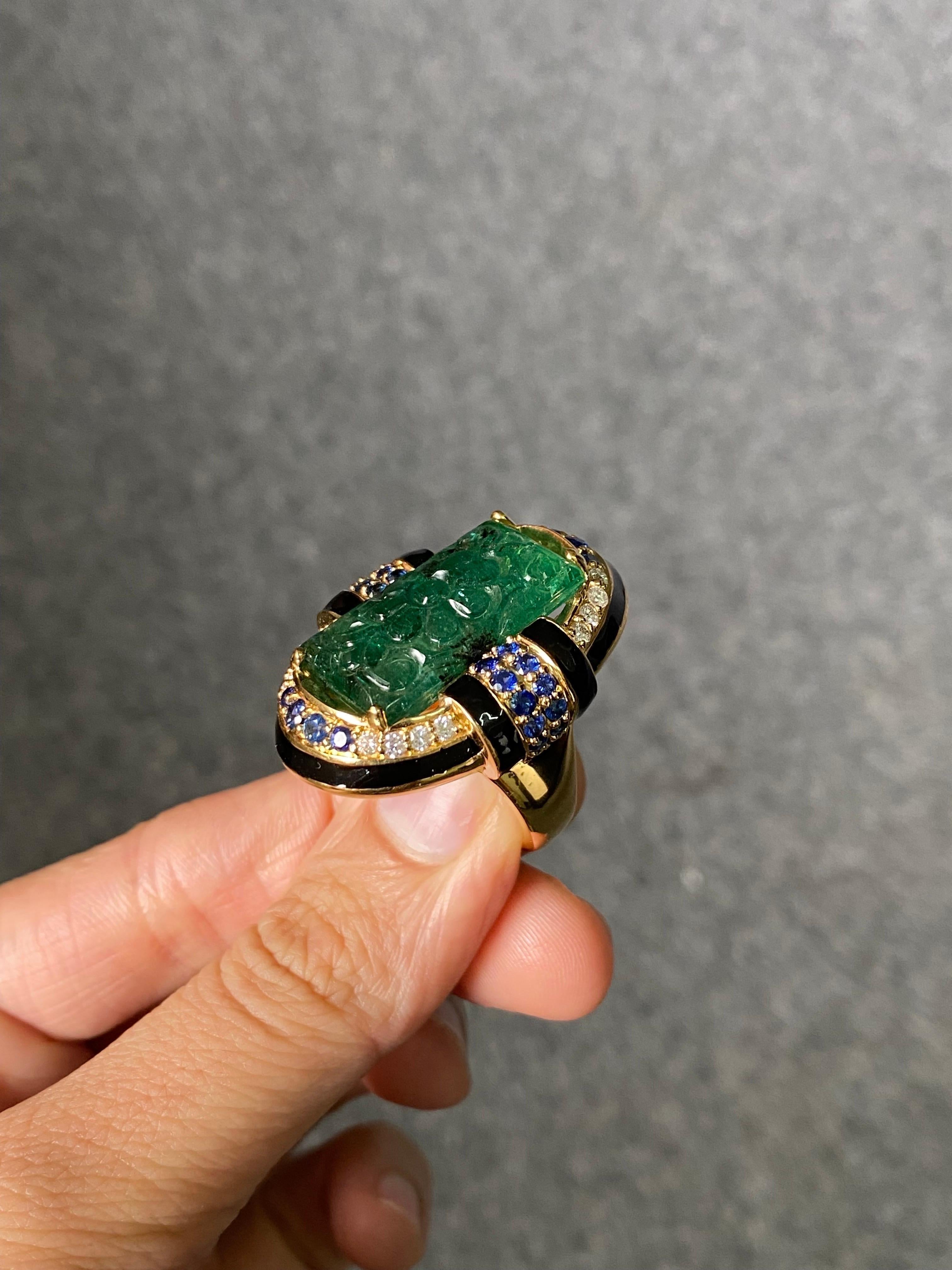 A beautiful art-deco inspired cocktail ring, with a 18.20 carat natural carved, vivid green Zambian Emerald, Blue Sapphire and White Diamond. The gemstones are set in solid 18K Yellow Gold, and black enamel is used to create the unique art-deco