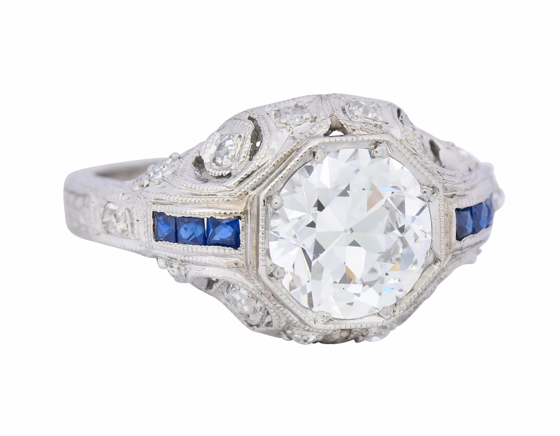 Centering a transitional cut diamond weighing 1.50 carat, F color and SI1 clarity

Set in a hexagonal mount flanked by channel set French cut sapphire weighing 0.15 carat total, dark royal blue in color

Accented by single cut diamonds weighing