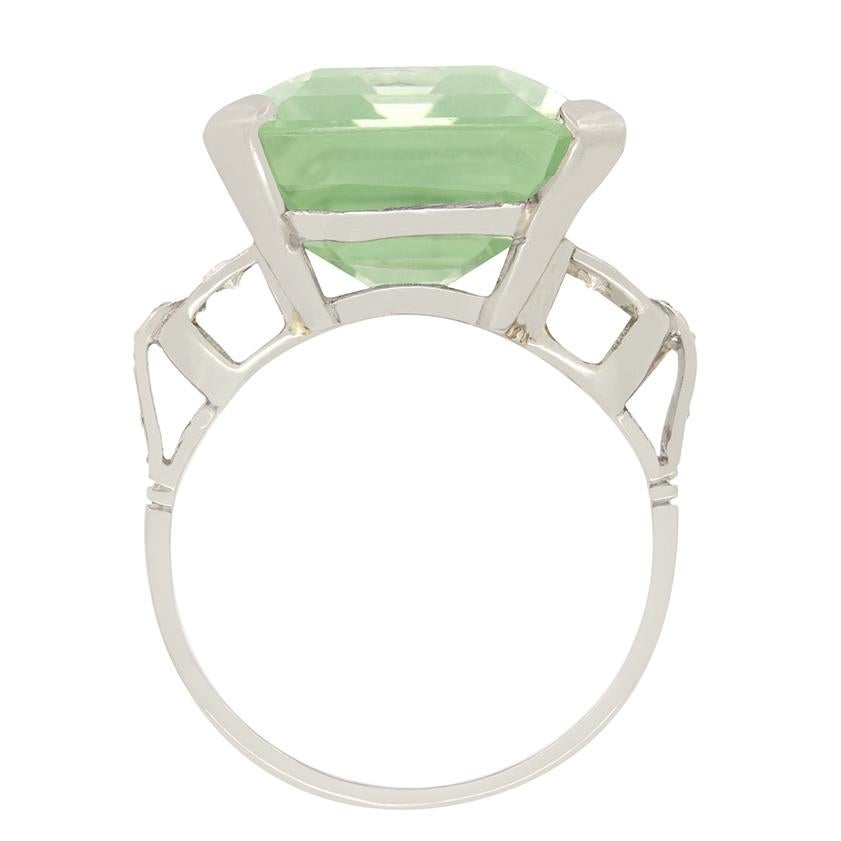 Cette bague de cocktail Art déco présente en son centre une remarquable aigue-marine de 18,52 carats taillée en émeraude, d'une teinte verte captivante. La grande aigue-marine verte est élégamment sertie à l'intérieur d'un panier ouvert, ce qui